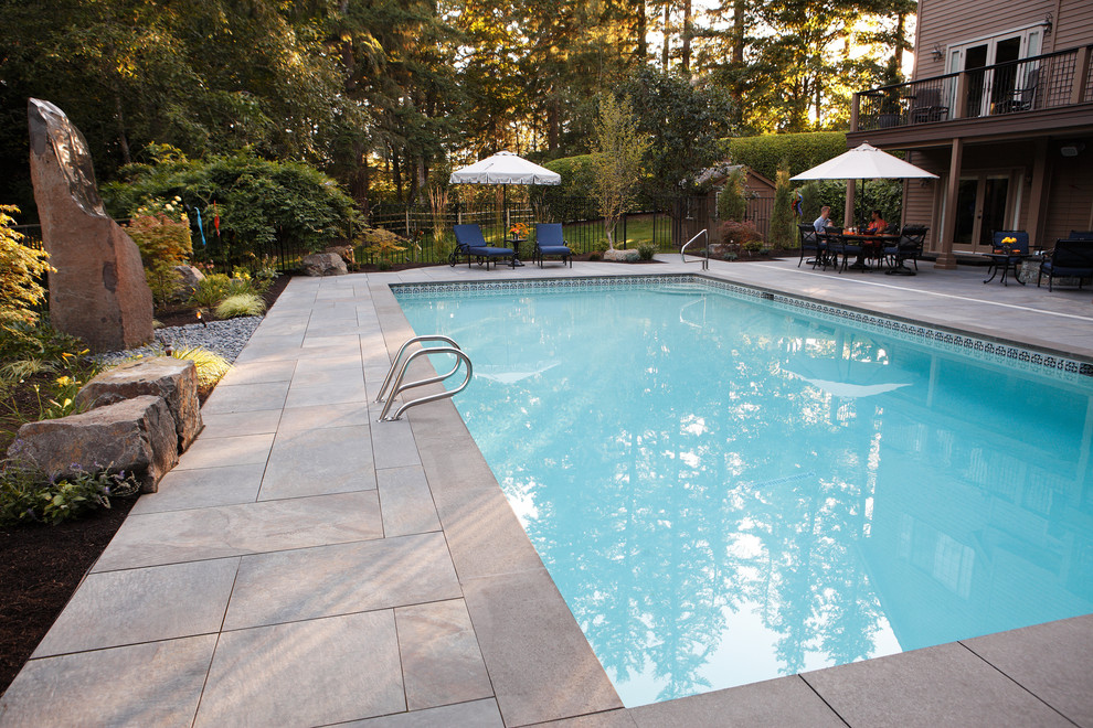 Immagine di una grande piscina monocorsia design rettangolare dietro casa con fontane e pavimentazioni in pietra naturale