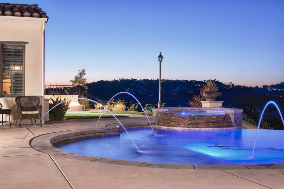 Ispirazione per una grande piscina a sfioro infinito design personalizzata dietro casa con fontane e pavimentazioni in cemento