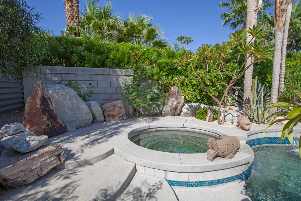 Foto di un'ampia piscina naturale moderna rotonda dietro casa con una vasca idromassaggio e lastre di cemento