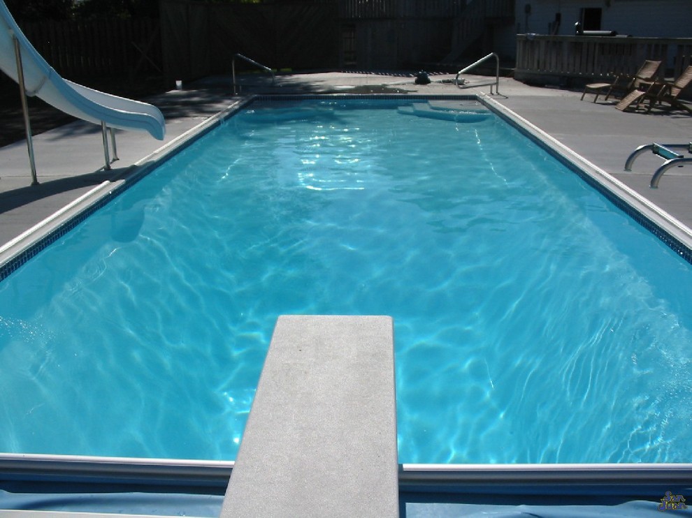 Ejemplo de piscina con tobogán alargada clásica de tamaño medio rectangular en patio trasero con adoquines de hormigón