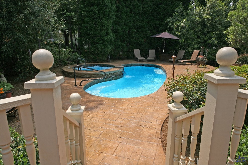 Modelo de piscinas y jacuzzis clásicos renovados de tamaño medio tipo riñón en patio trasero con suelo de hormigón estampado