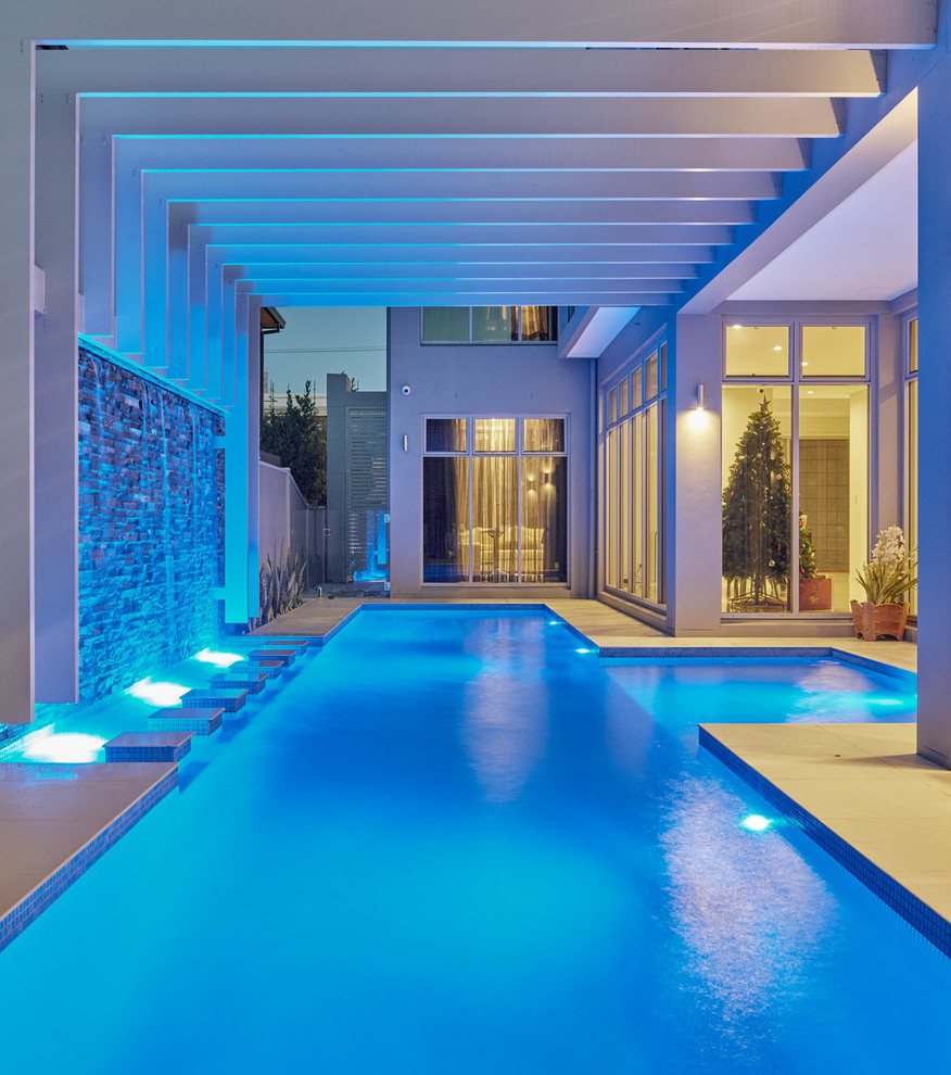 Ejemplo de piscina con fuente alargada actual de tamaño medio rectangular en patio trasero con adoquines de hormigón