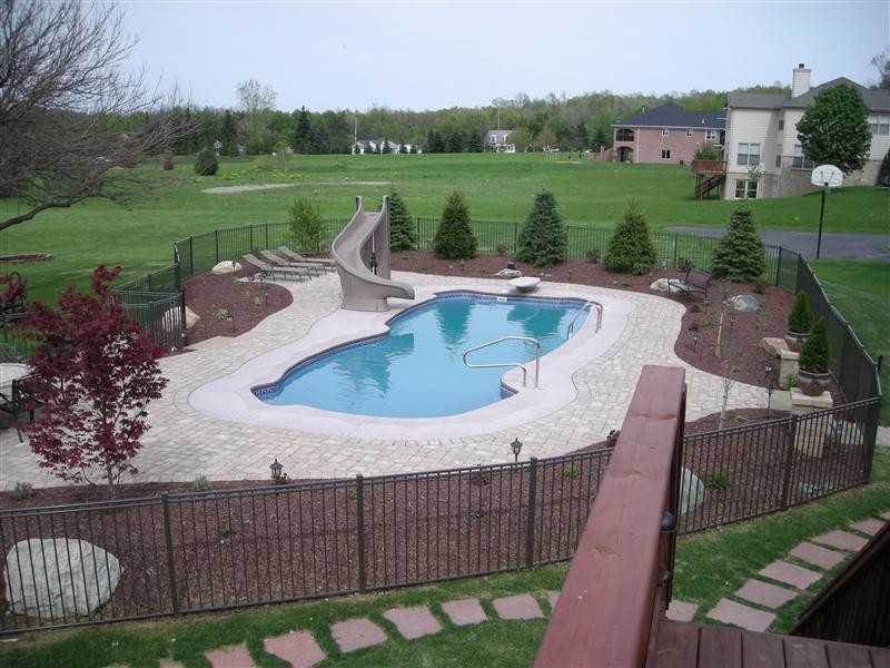 Modelo de piscina con tobogán clásica de tamaño medio a medida en patio lateral con suelo de hormigón estampado