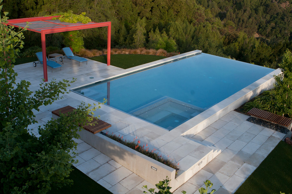 Diseño de piscina infinita actual grande rectangular en patio trasero con adoquines de piedra natural
