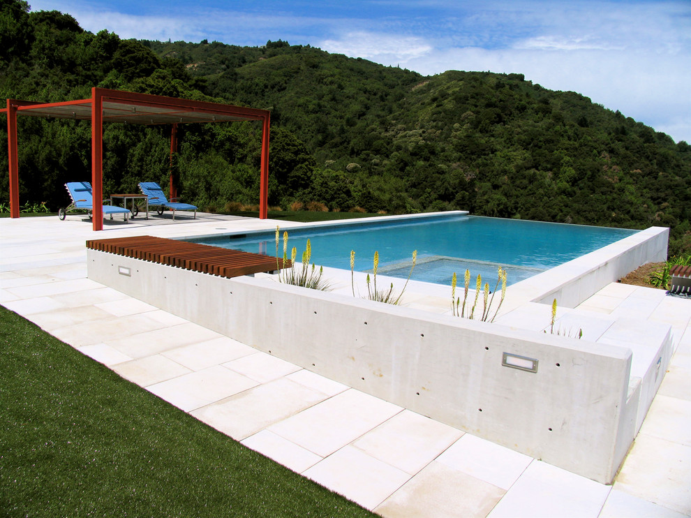 На фото: большой прямоугольный бассейн-инфинити на заднем дворе в современном стиле с покрытием из каменной брусчатки с