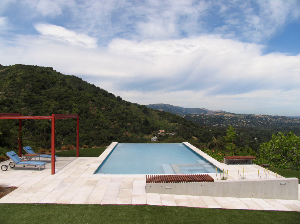 Ejemplo de piscina infinita actual grande rectangular en patio trasero con adoquines de piedra natural