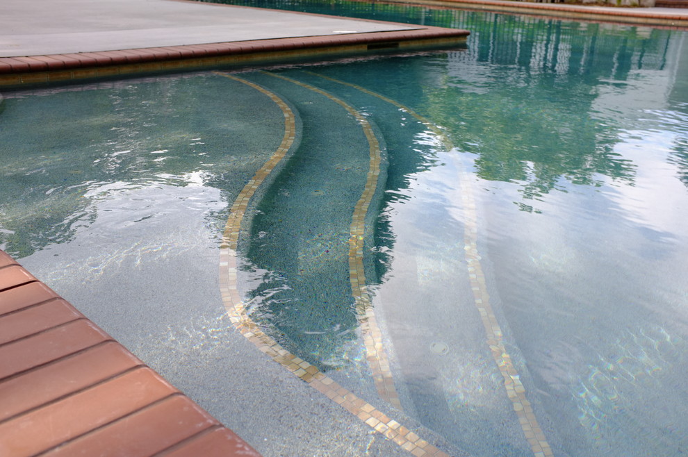 На фото: большой угловой бассейн на заднем дворе в современном стиле с домиком у бассейна и покрытием из каменной брусчатки с
