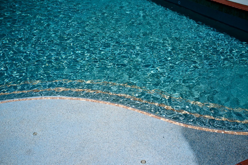 Modern inredning av en stor l-formad pool på baksidan av huset, med poolhus och naturstensplattor