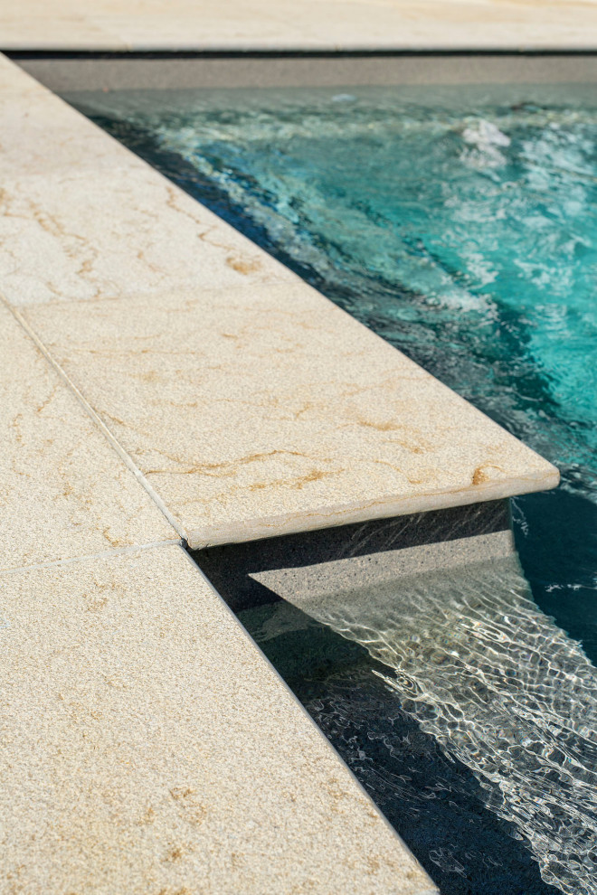 Ejemplo de piscina alargada costera de tamaño medio rectangular en patio trasero con paisajismo de piscina y adoquines de piedra natural