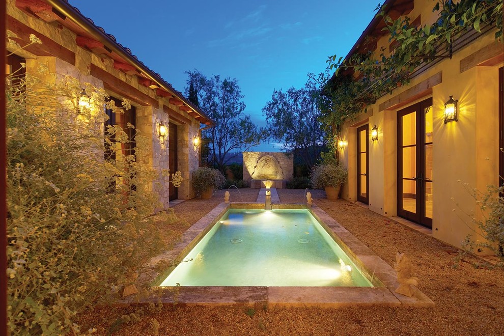 This is an example of a mediterranean courtyard rectangular swimming pool in Orange County with gravel and a water feature.