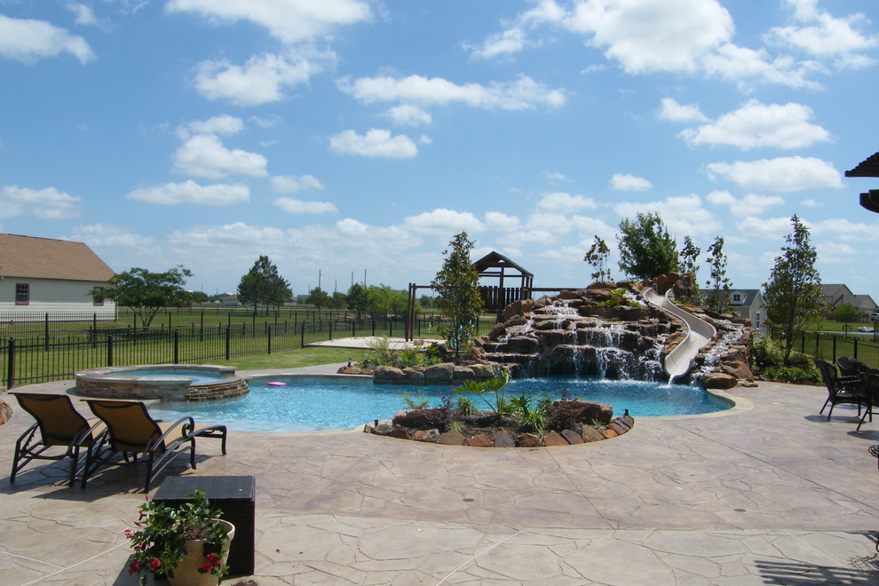 Immagine di una grande piscina stile rurale personalizzata dietro casa con un acquascivolo e cemento stampato