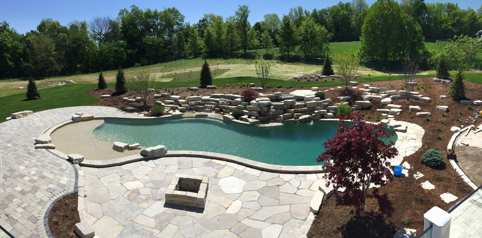 This is an example of an expansive modern back custom shaped natural swimming pool in Grand Rapids with a water feature and natural stone paving.