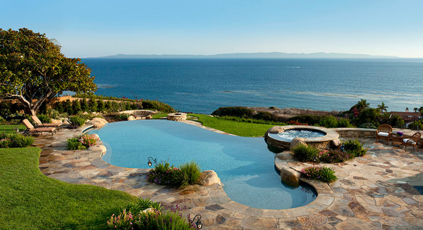 Foto di una grande piscina a sfioro infinito chic personalizzata dietro casa con pavimentazioni in pietra naturale e una vasca idromassaggio
