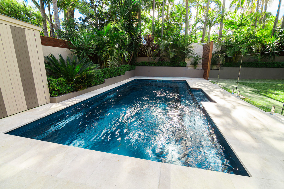 Diseño de piscina tropical de tamaño medio rectangular en patio trasero con suelo de baldosas