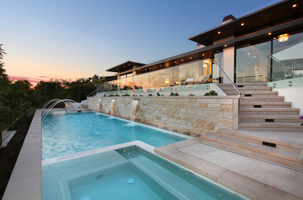 Idee per una piscina a sfioro infinito design rettangolare dietro casa e di medie dimensioni con pavimentazioni in pietra naturale e una vasca idromassaggio