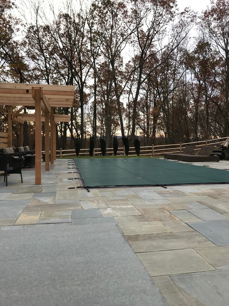 This is an example of a contemporary back rectangular natural hot tub in New York with natural stone paving.