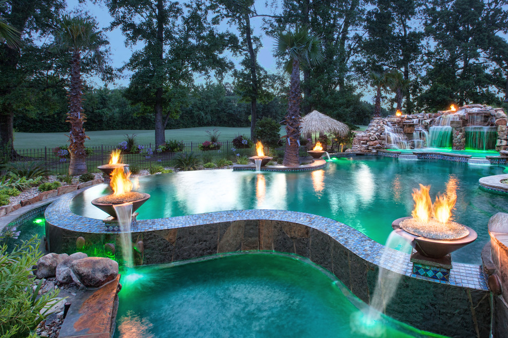 Idee per un'ampia piscina a sfioro infinito tropicale personalizzata dietro casa con pavimentazioni in pietra naturale e una vasca idromassaggio