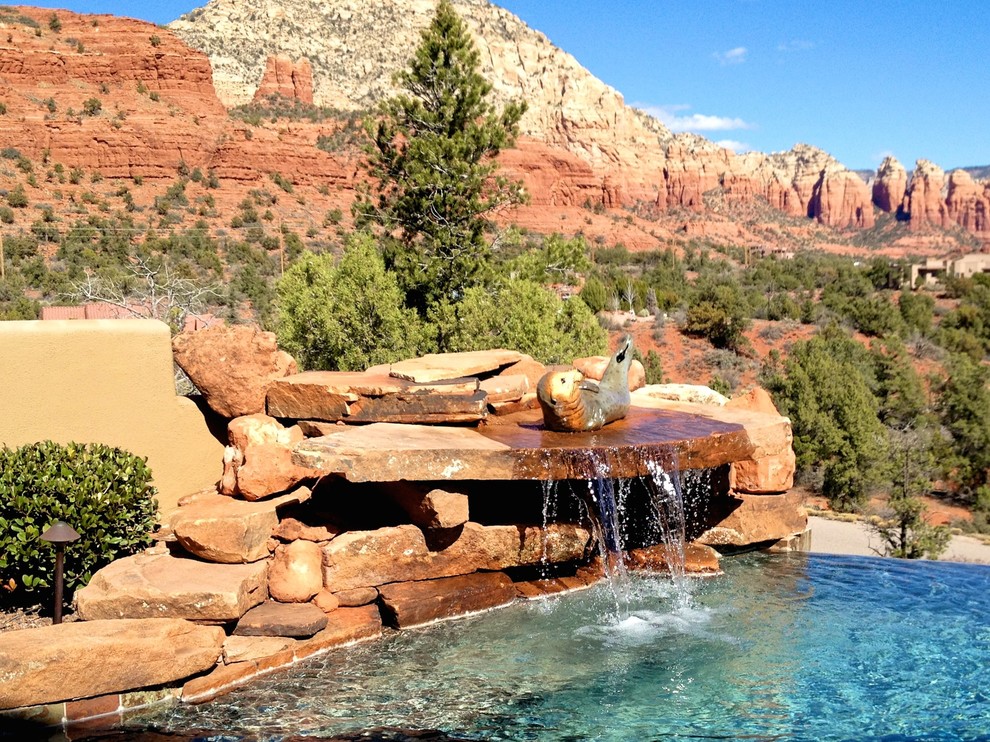 Cette photo montre une grande piscine arrière sud-ouest américain sur mesure avec un point d'eau et des pavés en pierre naturelle.