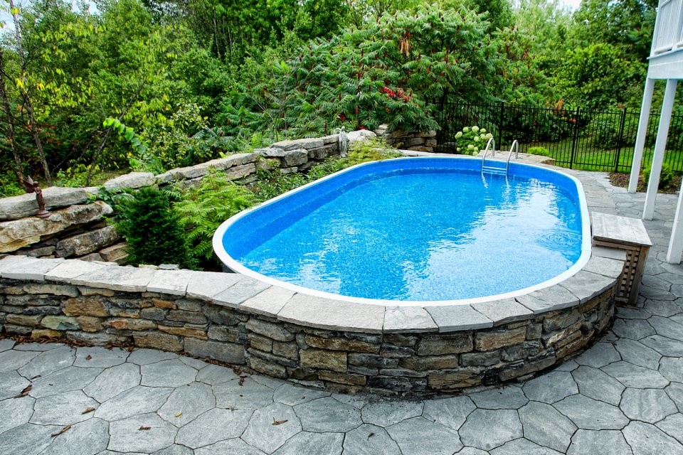 Imagen de piscina elevada tradicional de tamaño medio redondeada en patio trasero con adoquines de piedra natural