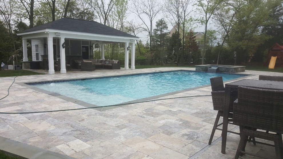 Diseño de piscina con fuente alargada actual grande rectangular en patio trasero con adoquines de piedra natural