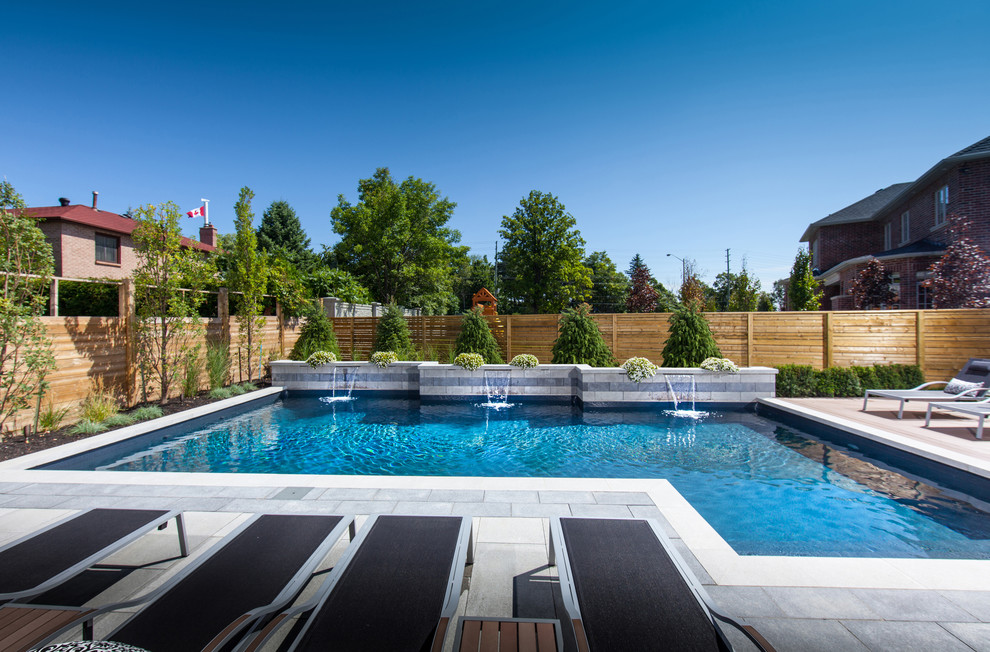 Foto de piscina con fuente alargada actual de tamaño medio en forma de L en patio trasero con adoquines de piedra natural
