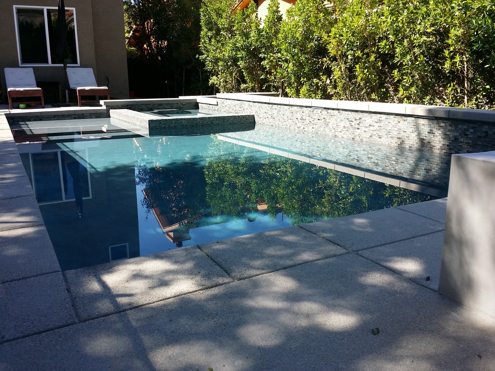 Imagen de piscina con fuente moderna de tamaño medio rectangular en patio trasero con adoquines de hormigón
