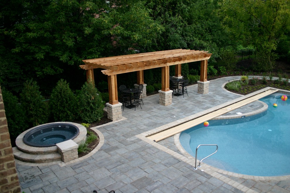 Immagine di una grande piscina chic a "C" dietro casa con pavimentazioni in cemento e una vasca idromassaggio