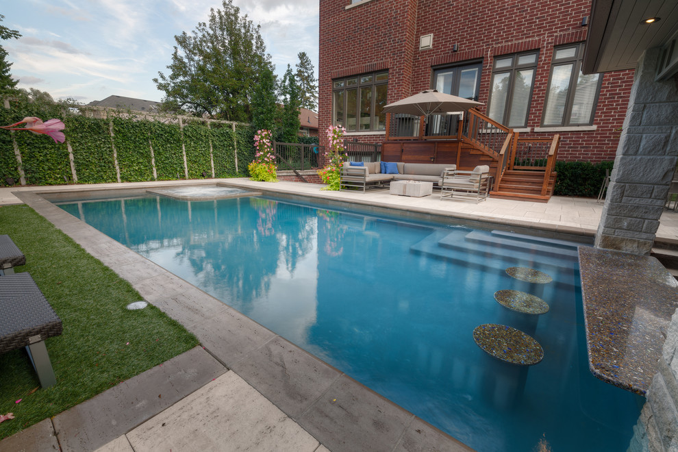 Cette image montre une grande piscine arrière minimaliste rectangle avec un point d'eau et des pavés en pierre naturelle.