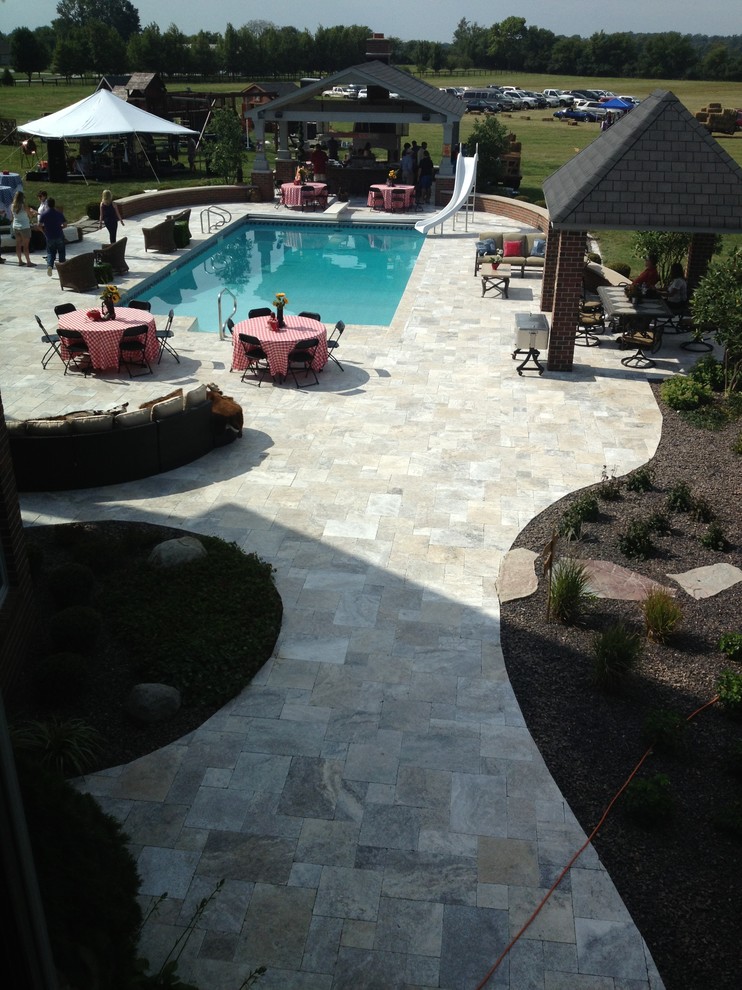 Modelo de piscina alargada rústica de tamaño medio rectangular en patio trasero con adoquines de piedra natural
