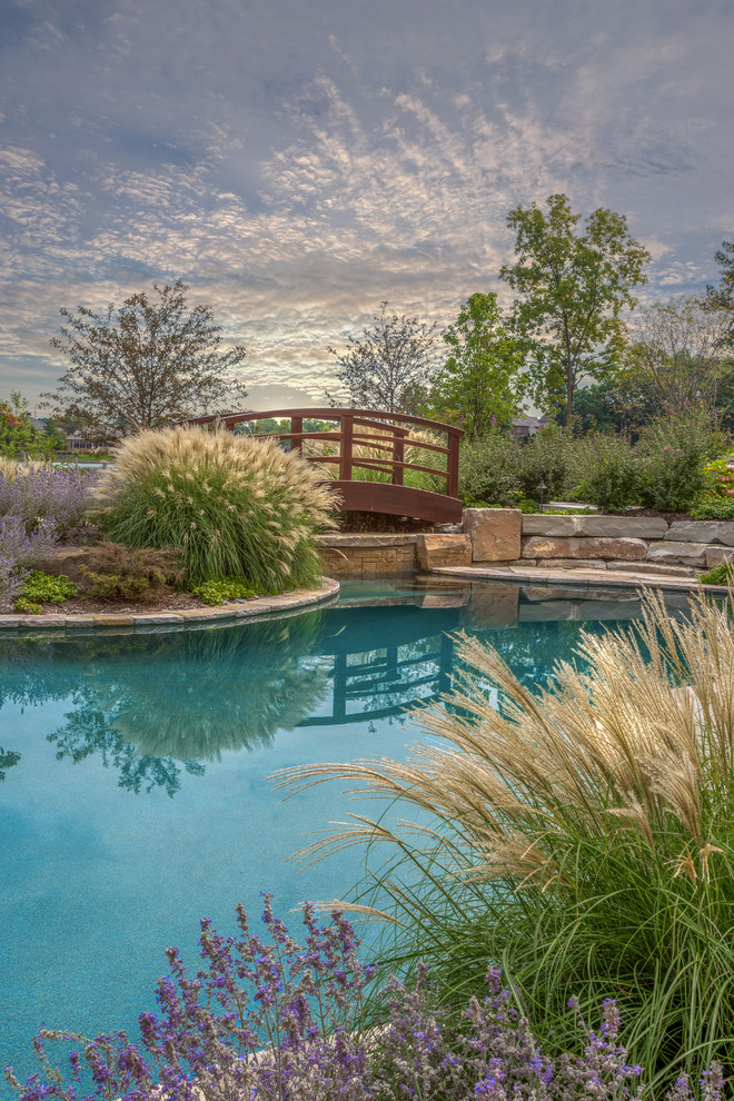 Cette image montre une grande piscine naturelle et arrière marine sur mesure avec un bain bouillonnant et des pavés en pierre naturelle.