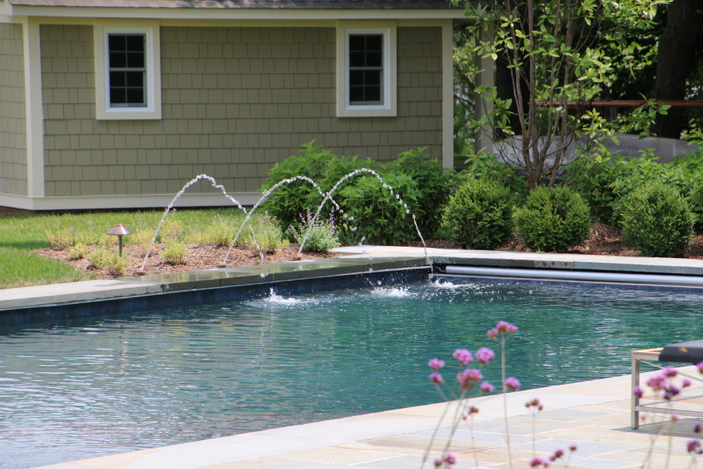 Modelo de piscina tradicional grande rectangular en patio trasero con adoquines de piedra natural