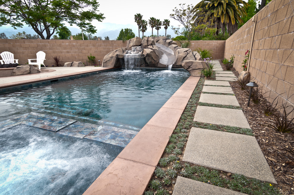Ejemplo de piscina con tobogán alargada exótica de tamaño medio rectangular en patio trasero con losas de hormigón