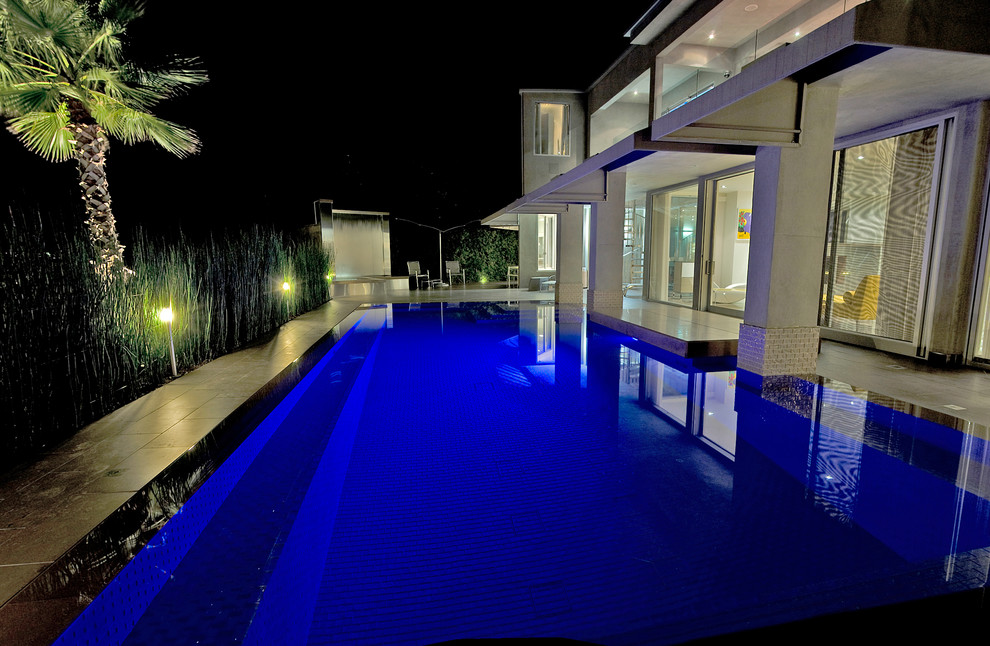 Immagine di una grande piscina a sfioro infinito minimal personalizzata dietro casa con pavimentazioni in pietra naturale