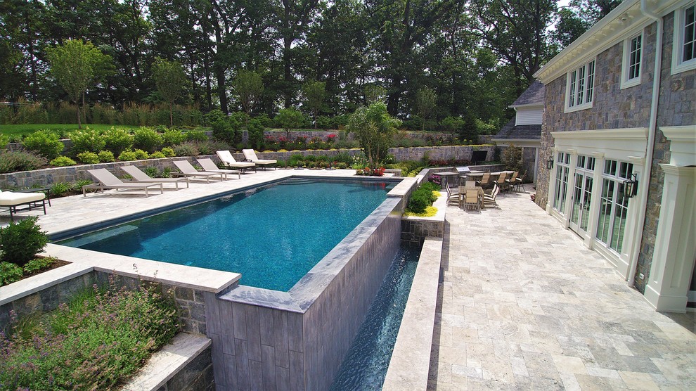 Large modern back rectangular infinity swimming pool in New York with a pool house and natural stone paving.