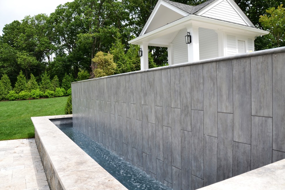 Foto di una grande piscina a sfioro infinito minimalista rettangolare dietro casa con una dépendance a bordo piscina e pavimentazioni in pietra naturale