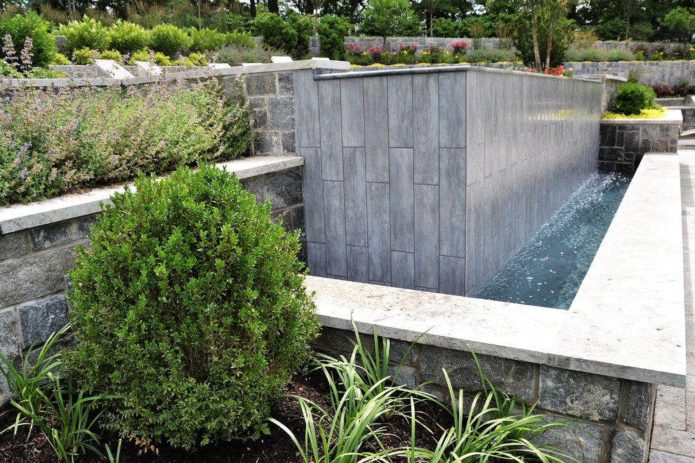 Immagine di una grande piscina a sfioro infinito minimalista rettangolare dietro casa con una dépendance a bordo piscina e pavimentazioni in pietra naturale