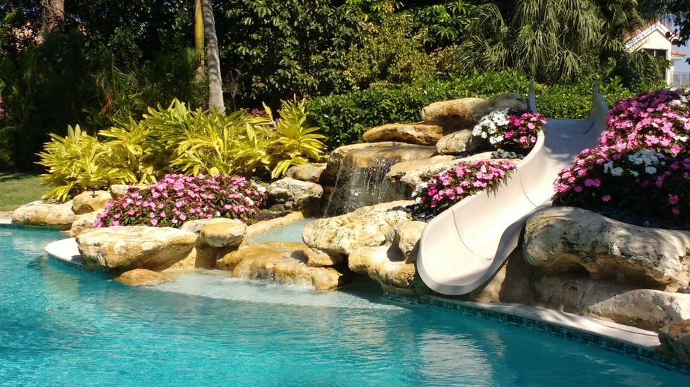 Immagine di una grande piscina a sfioro infinito stile marinaro rettangolare dietro casa con un acquascivolo e pavimentazioni in pietra naturale