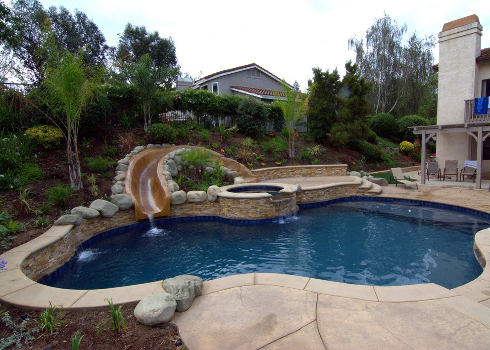 Diseño de piscina con tobogán natural exótica de tamaño medio a medida en patio trasero con suelo de hormigón estampado