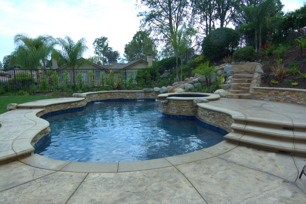 Inredning av en exotisk mellanstor anpassad pool på baksidan av huset, med vattenrutschkana och stämplad betong