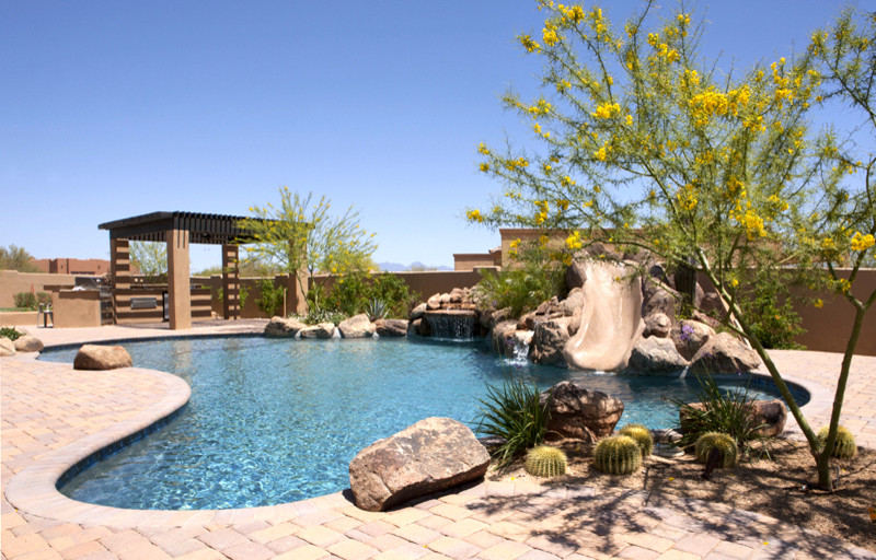Пример оригинального дизайна: естественный бассейн произвольной формы на заднем дворе в стиле рустика с водной горкой и мощением тротуарной плиткой