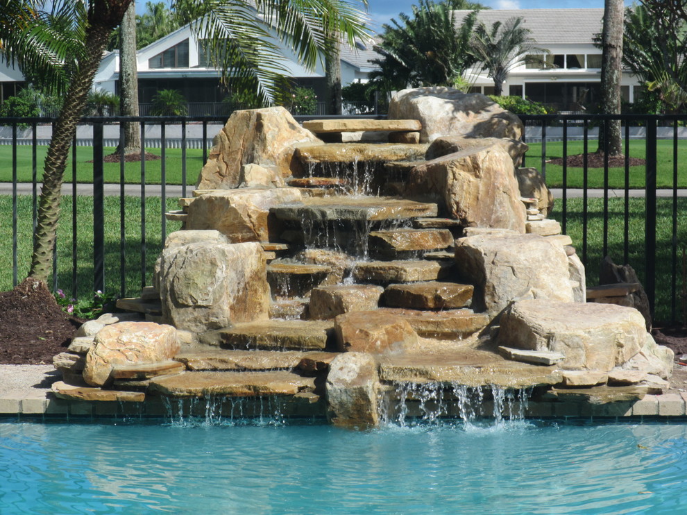 Diseño de piscina con fuente natural tropical grande en patio trasero