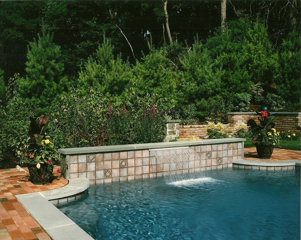 Ejemplo de piscina con fuente alargada tradicional de tamaño medio a medida en patio trasero con adoquines de ladrillo