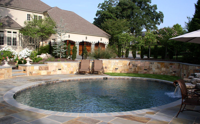 Diseño de piscina natural de estilo americano redondeada en patio trasero con adoquines de piedra natural
