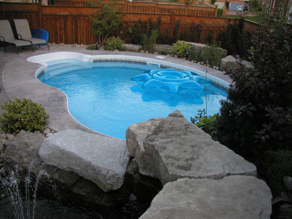 Cette image montre une petite piscine naturelle et arrière traditionnelle en forme de haricot avec un point d'eau et du béton estampé.