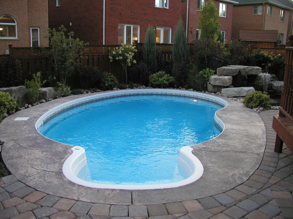 Modelo de piscina con fuente natural tradicional renovada pequeña tipo riñón en patio trasero con suelo de hormigón estampado