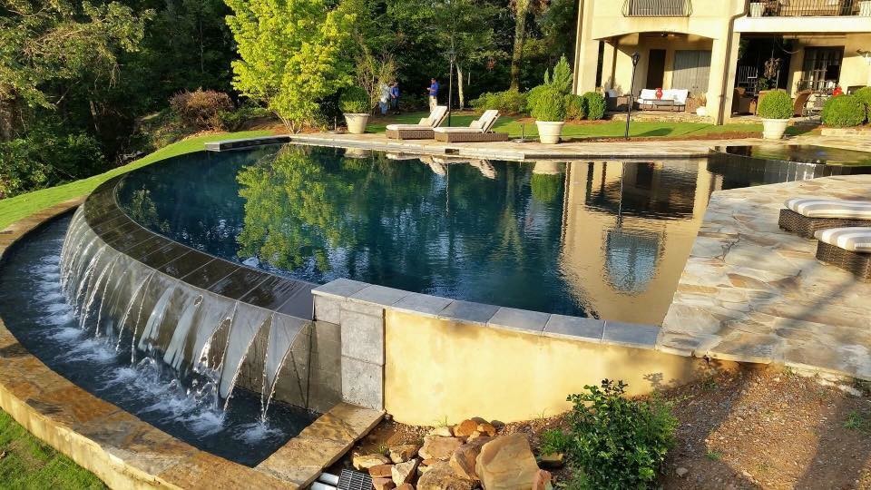 Immagine di una grande piscina a sfioro infinito minimal rotonda dietro casa con fontane e pavimentazioni in pietra naturale