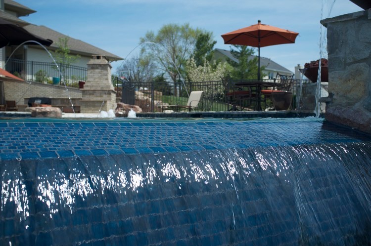 Esempio di un'ampia piscina a sfioro infinito tradizionale personalizzata dietro casa con un acquascivolo e pavimentazioni in pietra naturale