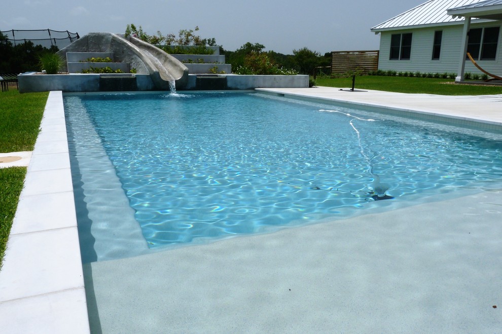 Inspiration för en stor funkis rektangulär pool på baksidan av huset, med vattenrutschkana och betongplatta