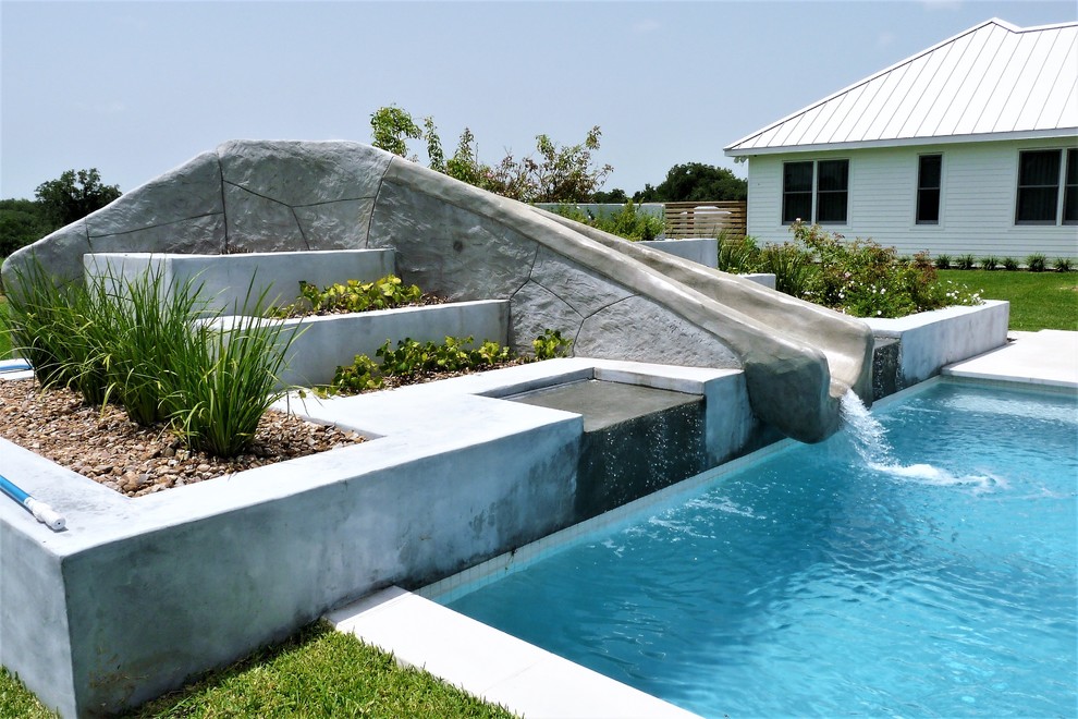 Bild på en stor funkis rektangulär pool på baksidan av huset, med vattenrutschkana och betongplatta