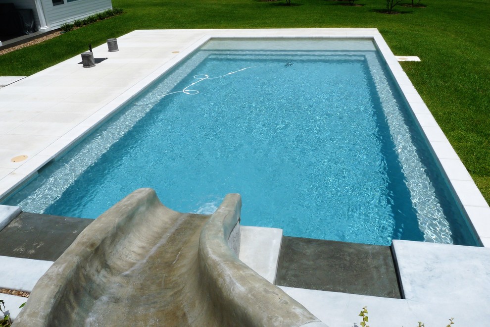 Idee per una grande piscina design rettangolare dietro casa con un acquascivolo e lastre di cemento